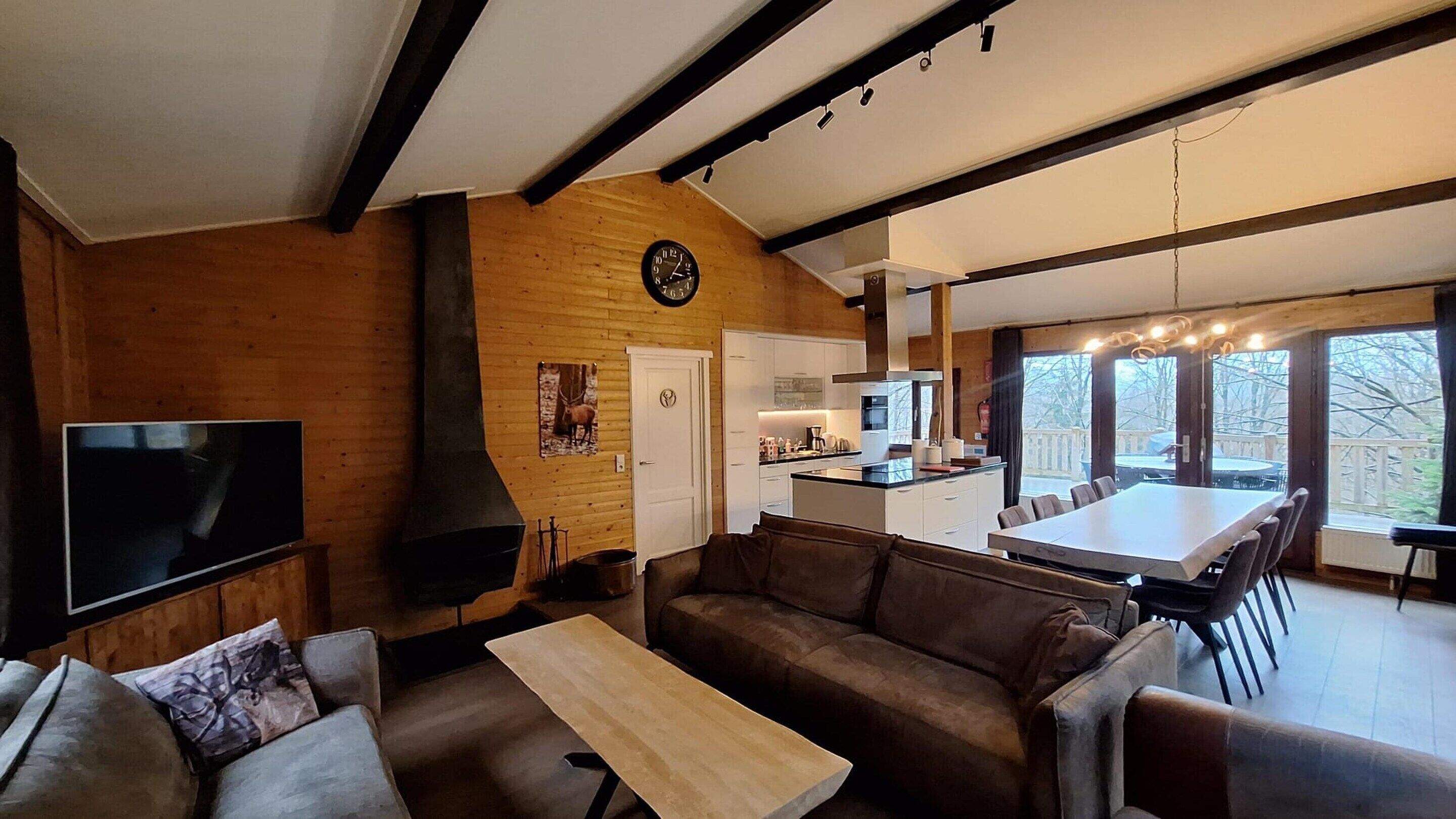 Ein modernes Wohnzimmer mit Kamin, Fernseher und Essbereich mit großem Tisch und Stühlen.