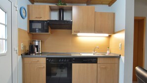 Una cucina compatta con mobili in legno, forno a microonde integrato, piano cottura e lavastoviglie.