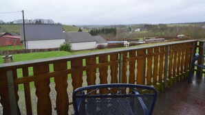 Un balcone con ringhiera in legno, una sedia in metallo e vista su un paesaggio rurale con case e campi.