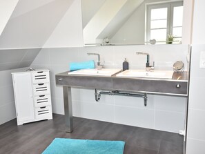 A modern bathroom with a dual sink vanity, a towel rack, and a mirror. - Ferienhaus in Gross Schwansee mit Sauna (Kalkhorst)