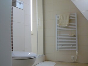 Un baño con inodoro blanco, cabina de ducha de vidrio y toallero blanco con toallas.