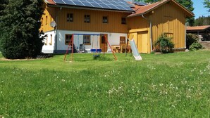 A two-story house with a solar panel roof, a swing set, and a slide in the yard.