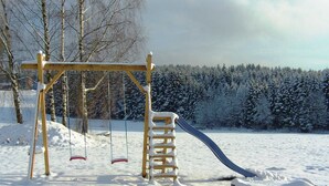 A wooden swing set in a snowy park with a slide.