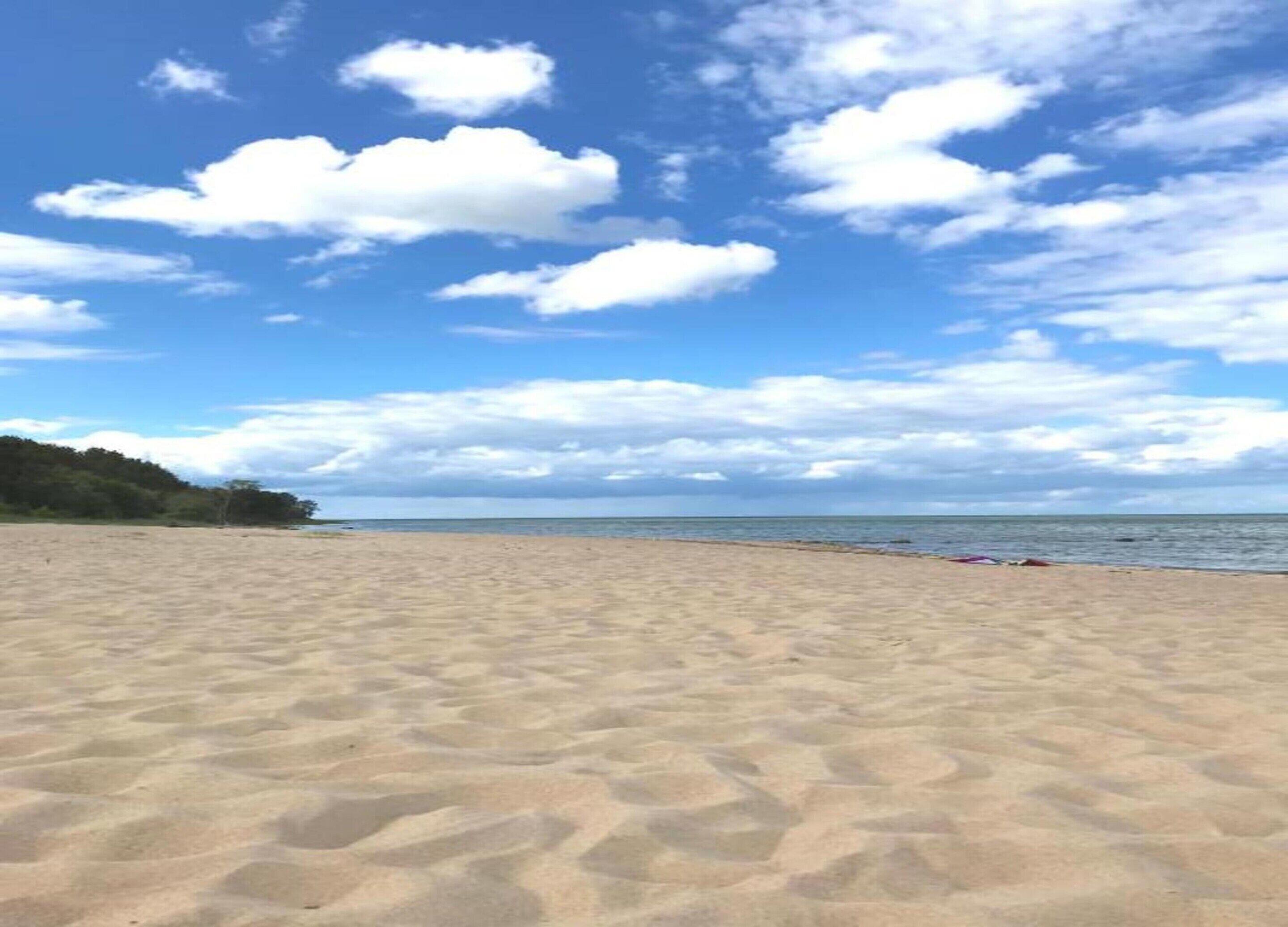 Una playa arenosa con cielo despejado y nubes dispersas.