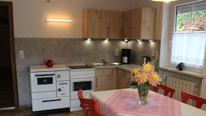 A compact kitchen with wooden cabinets, a white stove, and a sink. There's a table with a pink tablecloth and a vase of flowers. - Apartment in Goggersreut mit Terrasse (Roehrnbach)