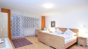 A bedroom with a wooden bed, a bedside table, a nightstand, a desk, a chair, a window with curtains, and a framed picture on the wall. - Apartment in Goggersreut mit Terrasse (Roehrnbach)