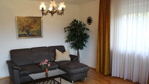 A living room with a dark grey sofa, a small coffee table, a potted plant, and a chandelier. - Apartment in Goggersreut mit Terrasse (Roehrnbach)