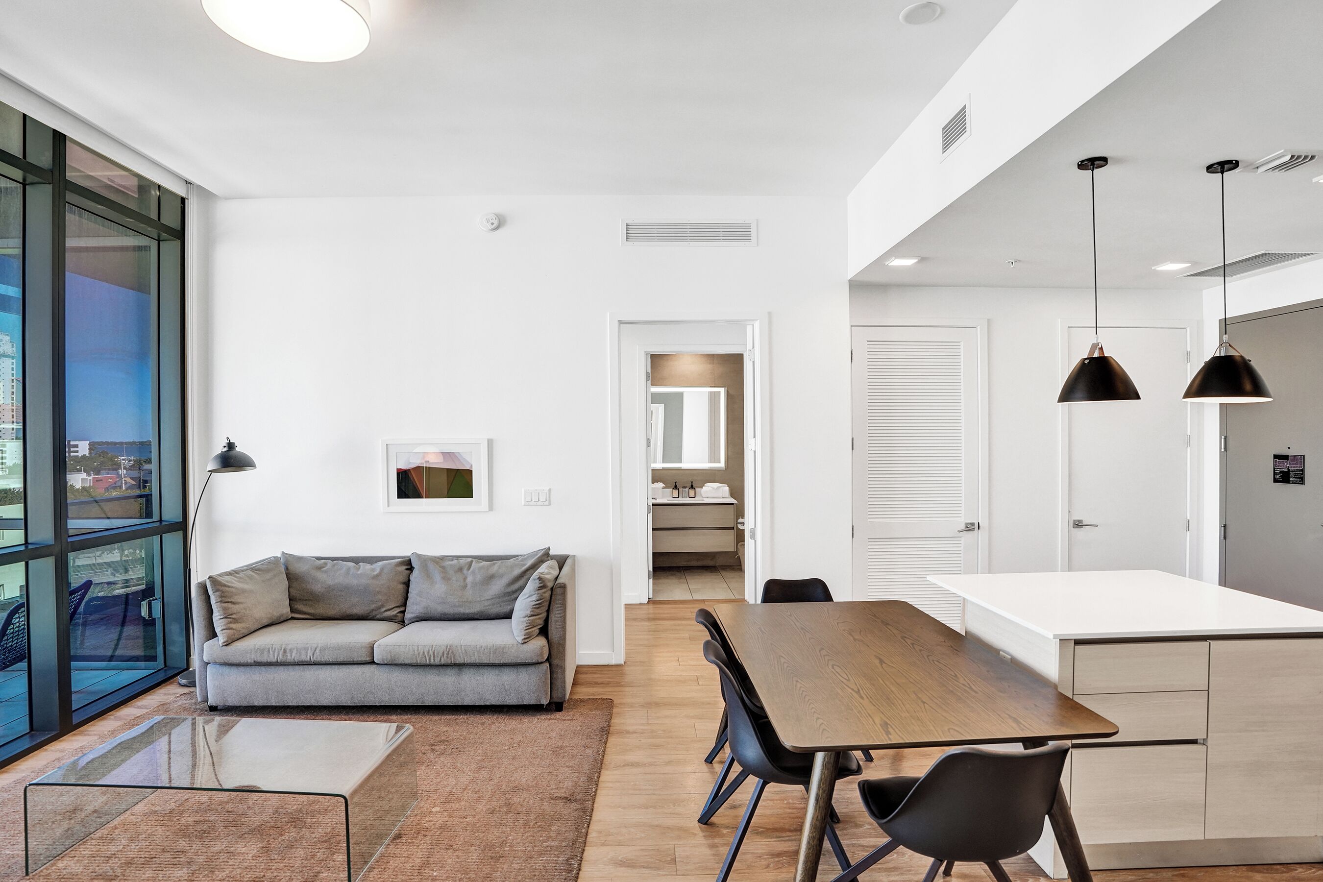A modern living room with a sofa, a dining table, and a kitchen area with cabinets and a refrigerator.