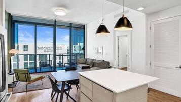Ein modernes Hotelzimmer mit großem Fenster, Essbereich, einer Couch und einer Küchenzeile.