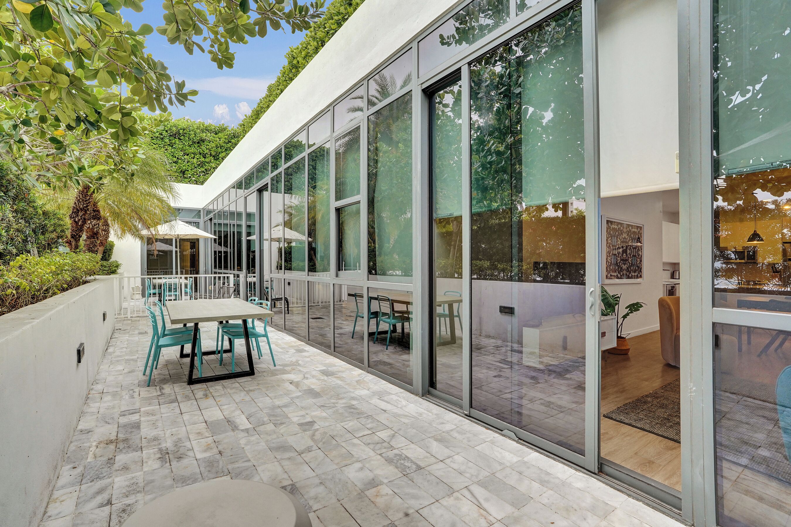 Een modern terras buiten met een glazen wand, zitplaatsen en uitzicht op het interieur.