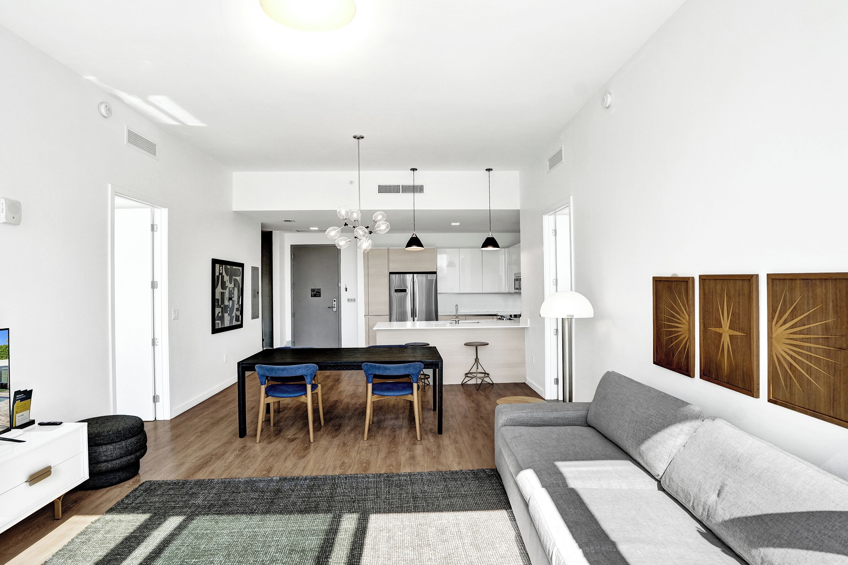 A modern living room with a sofa, a dining area with chairs, and a kitchen in the background.