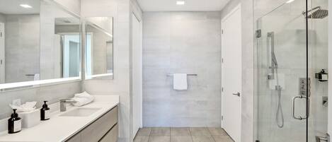 A modern bathroom with a large mirror, two sinks, a glass shower enclosure, and a towel hanging on the wall.