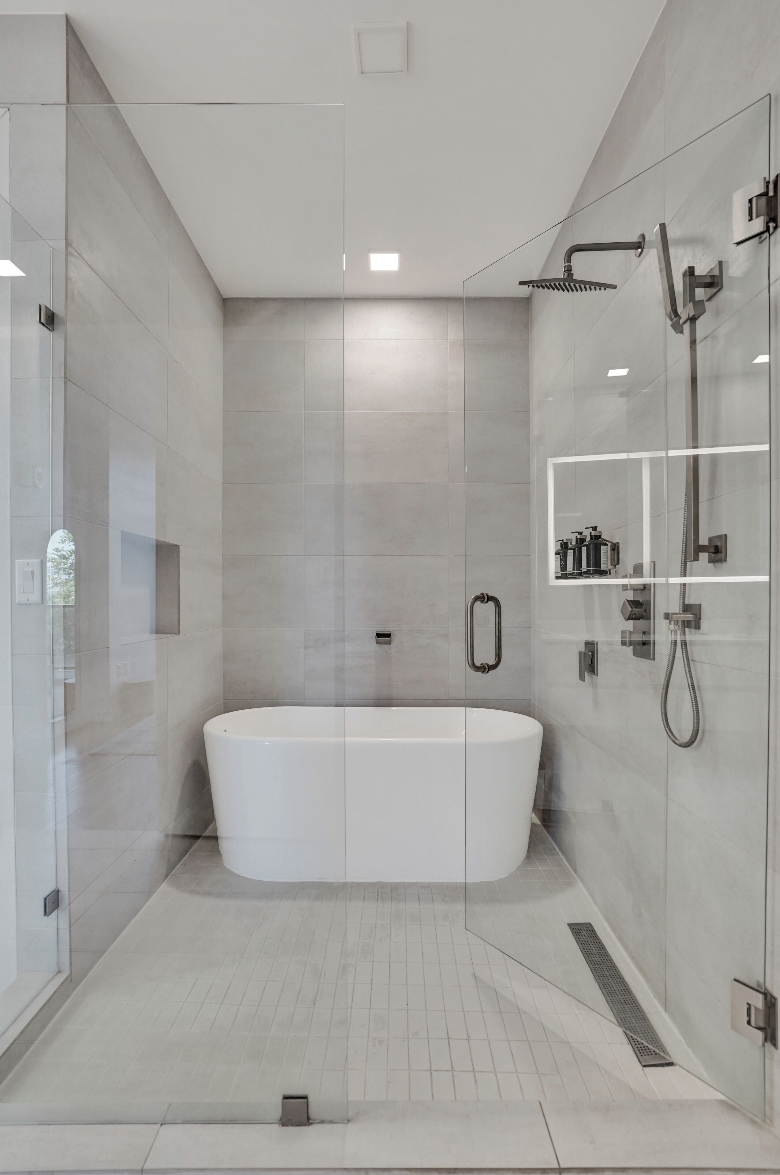 A modern bathroom with a freestanding bathtub, glass shower enclosure, and built-in storage shelves.