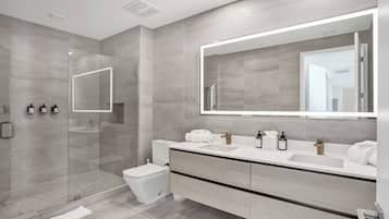 Un baño moderno con cabina de ducha de vidrio, inodoro, tocador con espejo grande y lavamanos.