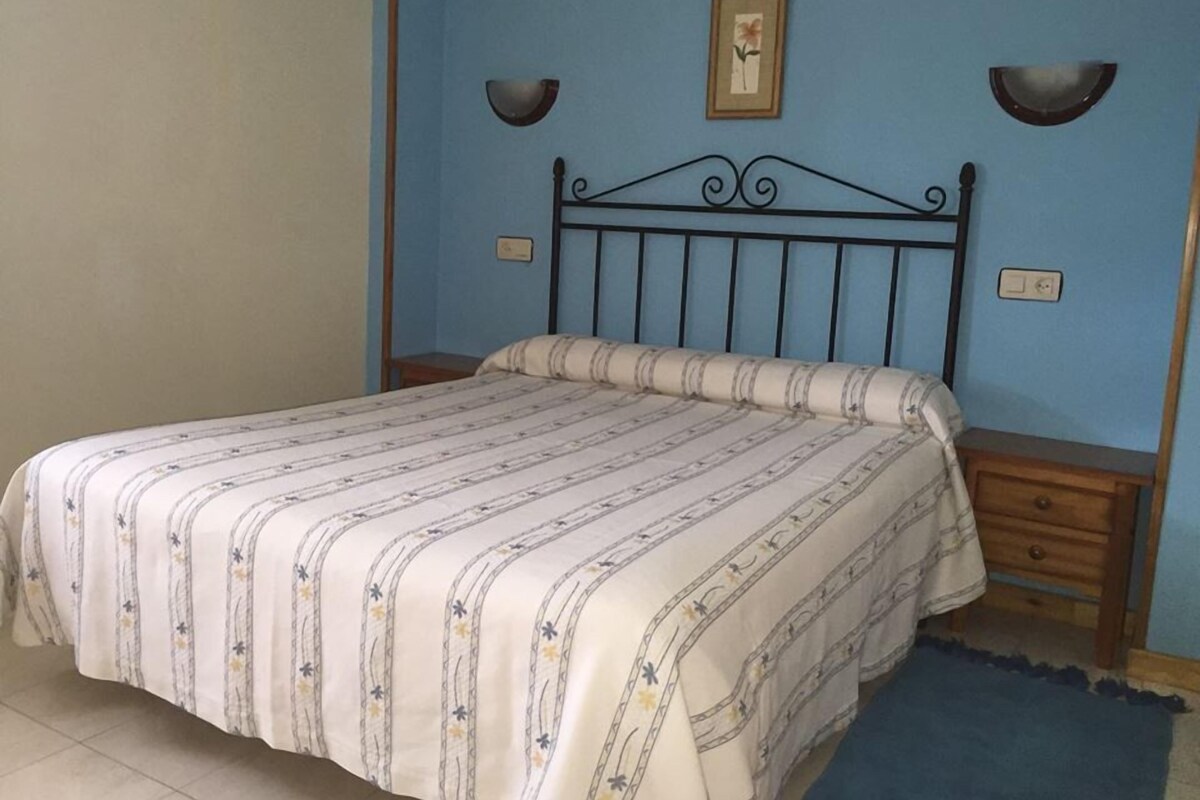 Une chambre à coucher comprenant un lit, une table de chevet, un luminaire fixé au mur et un tableau encadré accroché au mur.