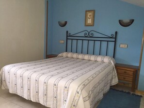 Une chambre à coucher comprenant un lit, une table de chevet, un luminaire fixé au mur et un tableau encadré accroché au mur.