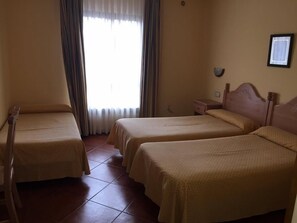 Une chambre d’hôtel avec deux lits simples, une table de chevet, une petite table et une fenêtre avec des rideaux.