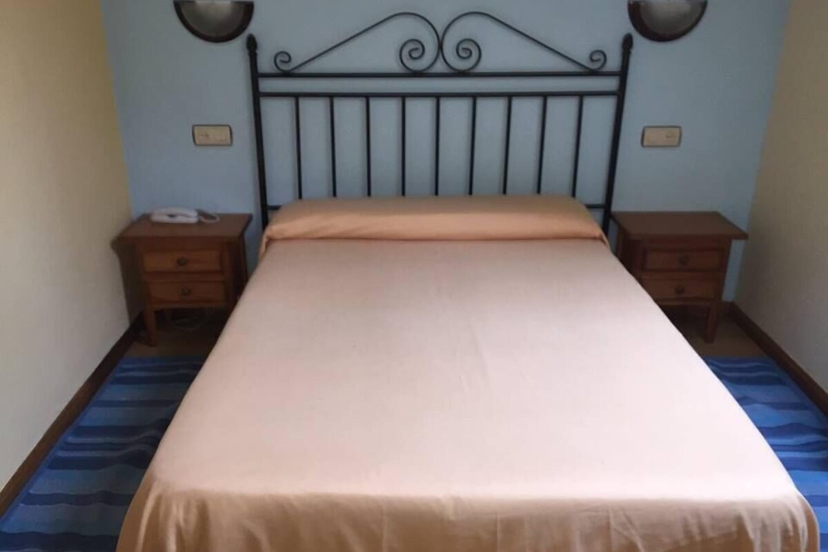 Une chambre à coucher avec un lit, deux tables de chevet, une lampe fixée au mur et un tableau encadré.