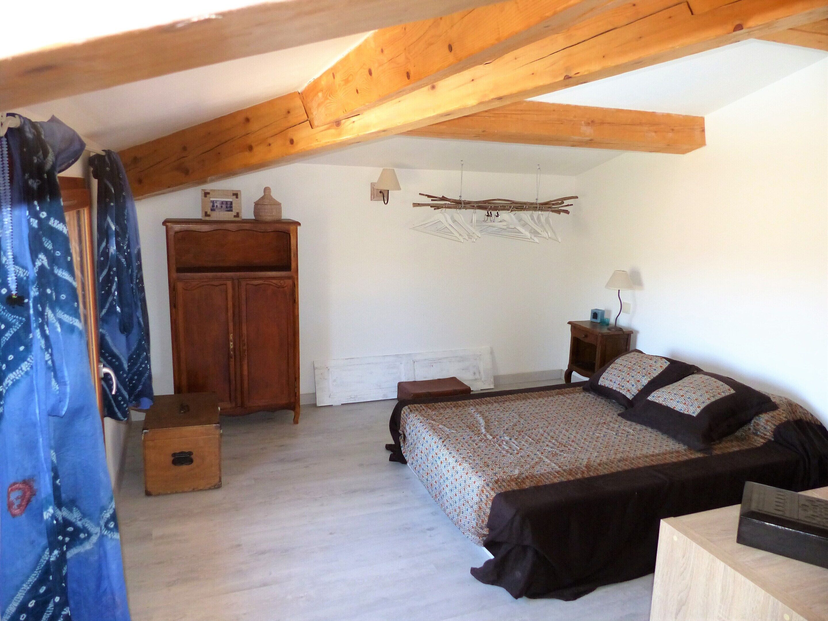 A bedroom with a wooden ceiling, a bed, a nightstand, a dresser, and a hanging clothes rack.