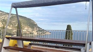 A wooden bench with a metal frame, a white railing, and a view of the sea and a hill. - Elegant Seaside Villa in Eze (Èze)