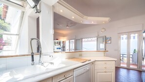 A kitchen with a built-in dishwasher, a sink with a faucet, a wooden countertop, and a ceiling fan. - Elegant Seaside Villa in Eze (Èze)