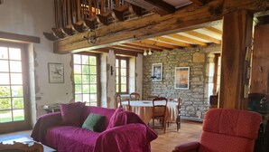 A rustic room with exposed wooden beams, a stone wall, a dining table with chairs, and a purple sofa. - Holiday Home Vault-de-lugny Near Forest (Vault-de-Lugny)