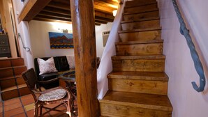 A wooden staircase with a white handrail, a black sofa with patterned cushions, and a rustic chair. - Casita G - 1 Bed, 1 Bath (Loft Style, Stairs) (Santa Fe)