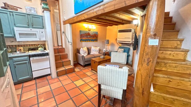 A compact kitchen with a stove, microwave, and cabinets. There is a living area with a sofa, a coffee table, and a painting on the wall. A wooden staircase leads to another level. - Casita G - 1 Bed, 1 Bath (Loft Style, Stairs) (Santa Fe)