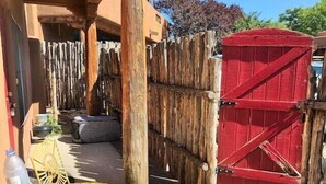 A wooden fence with a red gate, a yellow woven table, and a bottle on the ground. - Casita G - 1 Bed, 1 Bath (Loft Style, Stairs) (Santa Fe)