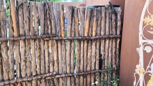 A rustic wooden fence with vertical planks and a decorative metal gate on the right. - Casita G - 1 Bed, 1 Bath (Loft Style, Stairs) (Santa Fe)