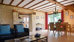 A living room with a sofa, a glass coffee table, and a dining area with wicker chairs and a table. - Nature Hideaway in St Germain du Pert (Saint-Germain-du-Pert)