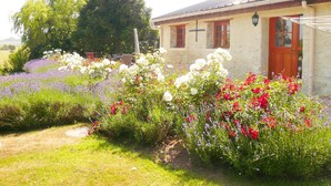 A stone building with a red door, a cross, and a garden with various flowers. - Nature Hideaway in St Germain du Pert (Saint-Germain-du-Pert)