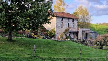 A stone house with a sloped roof, a covered porch, and a garden with various plants and trees.