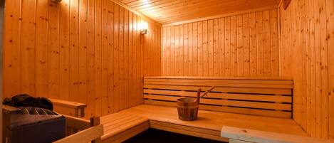 A wooden sauna with benches, a bucket, and a heater.
