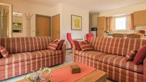 Una sala de estar con dos sofás a cuadros, una mesa de centro y un comedor con una silla roja.