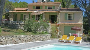 Una casa de dos pisos con fachada de piedra, una piscina y mobiliario exterior.
