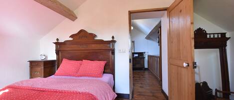 Un dormitorio con una cama de madera, una colcha roja con lunares, una mesita de noche de madera y una puerta de madera que da a otra habitación.