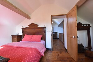 A bedroom with a wooden bed, a red polka dot bedspread, a wooden nightstand, and a wooden door leading to another room. - Cottage in France With Garden Near Lake (Montaron)