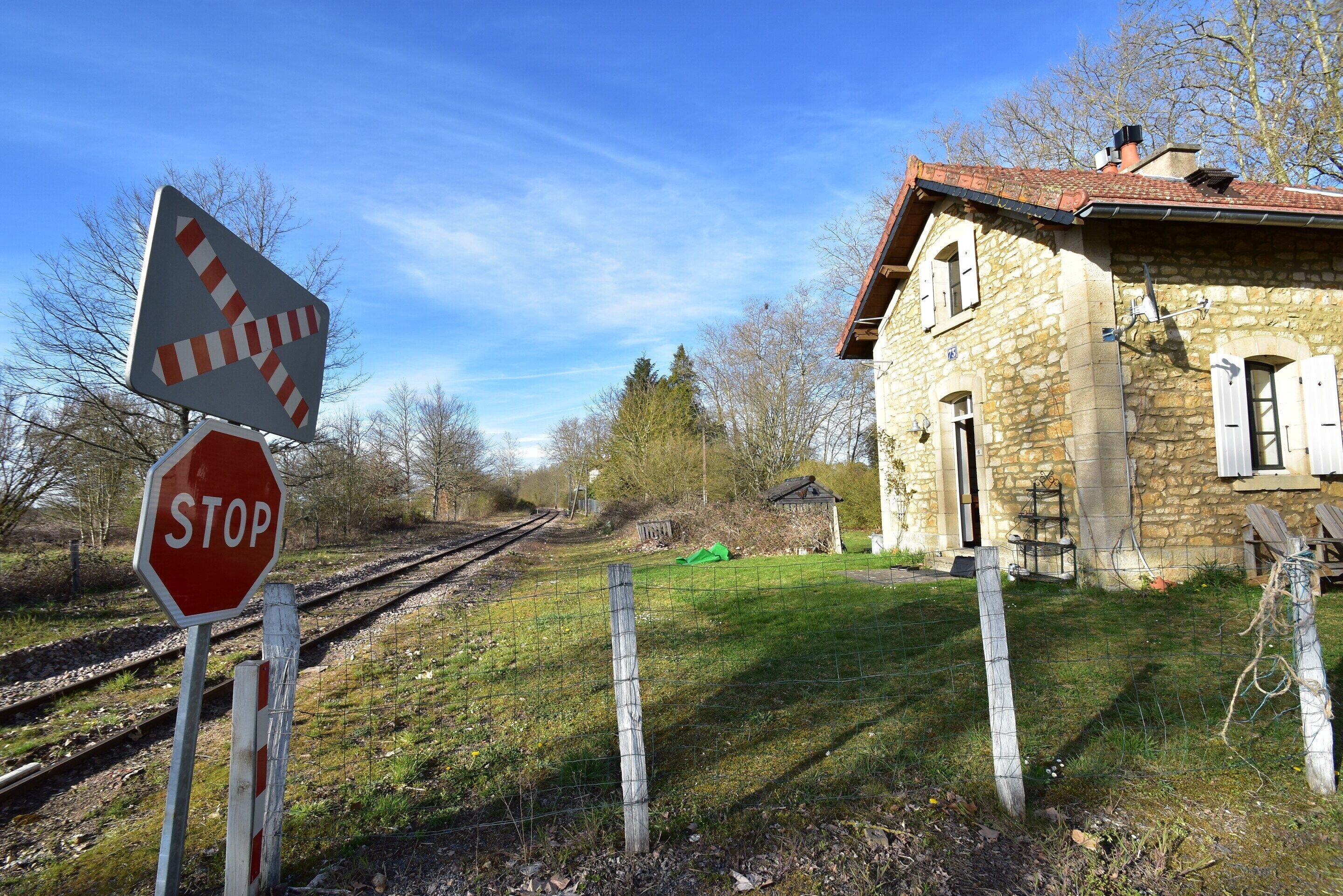 A rural setting with a stone building, railway tracks, and a stop sign.