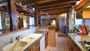 Une cuisine dotée d’un grand évier, de poutres en bois, de murs en pierre et d’une cuisinière à gaz.