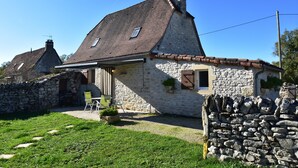 Une maison en pierre avec un toit en pente, un petit porche et un mur en pierre.