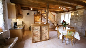 Une cuisine rustique avec des meubles en bois, un îlot central en briques et un coin repas comprenant une table et des chaises.