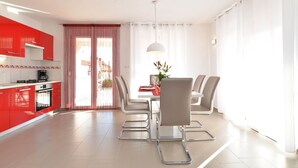 A modern kitchen with red cabinets, a dining area with a white table and grey chairs, and a large window with sheer curtains. - Villa 1771 (Vodnjan)