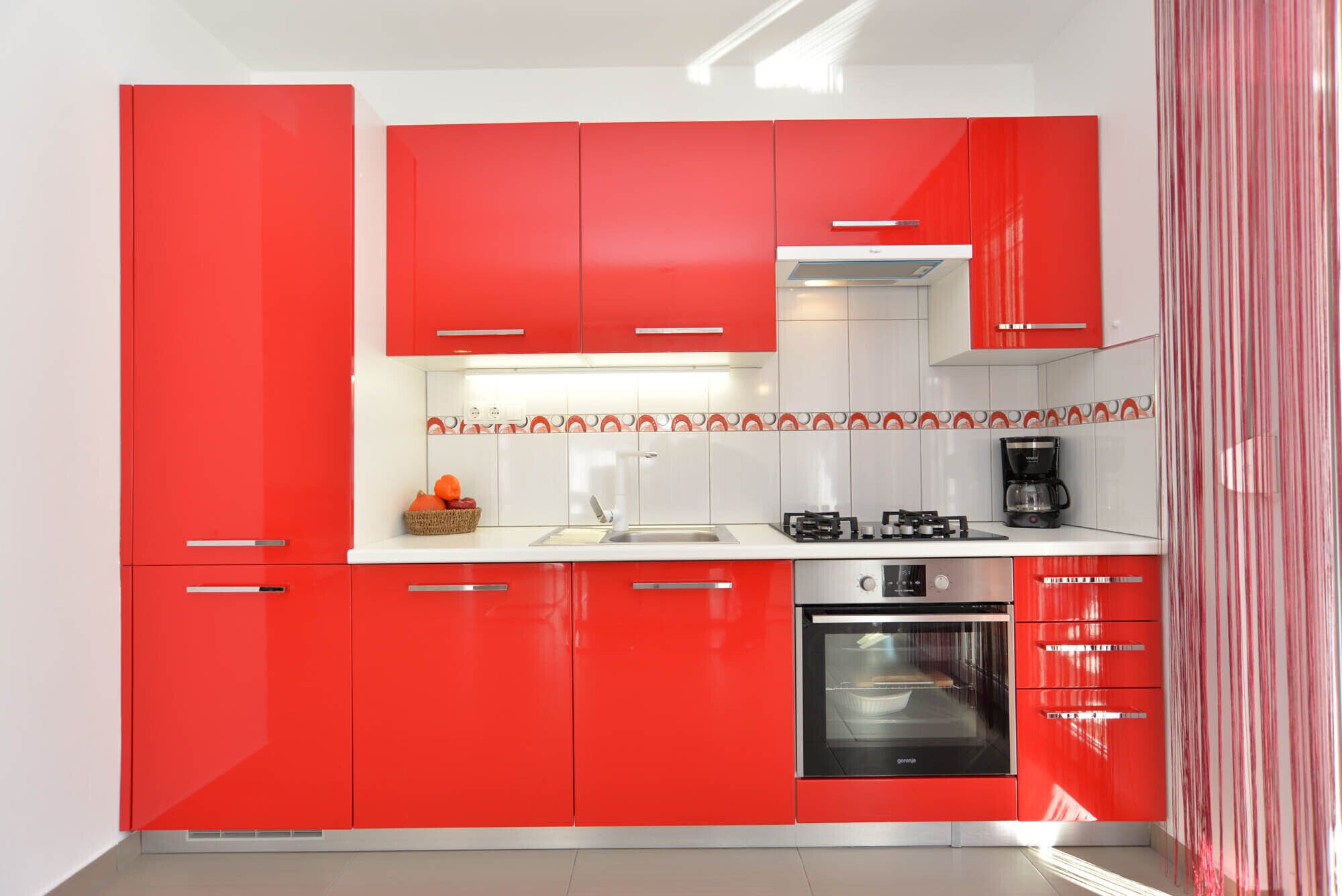 A modern kitchen with red cabinets, a built-in oven, and a coffee maker.