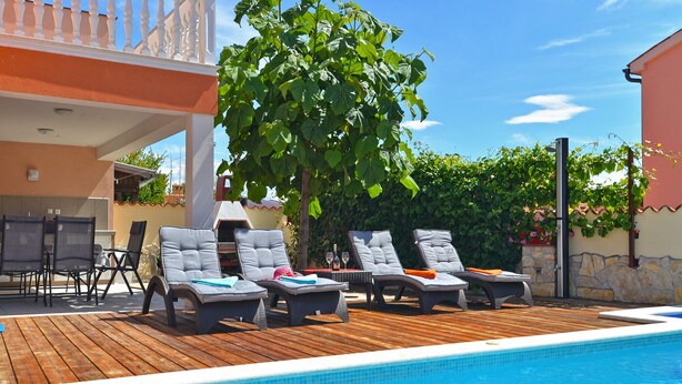 A poolside area with lounge chairs, a wooden deck, and a clear blue pool. - Villa 1771 (Vodnjan)