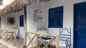 Una habitación con techo de paja, pared blanca, puerta azul y cama con estructura metálica.