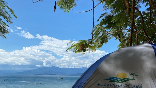 Una playa con una carpa identificada como 'Maravilha de Ará Camping & Pousada' y una mesa blanca.