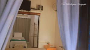Un dormitorio con cama, una mesita de noche con lámpara, televisor y puerta que da a otra habitación.