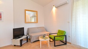 Una stanza piccola e luminosa con un letto, una poltrona verde, una TV su un mobile e uno specchio appeso al muro.