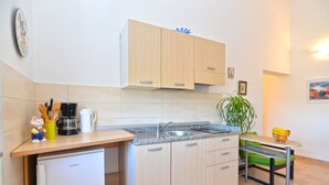 Una cucina compatta con lavello, piccolo frigorifero, mobili in legno, una sedia verde e una pianta in vaso.